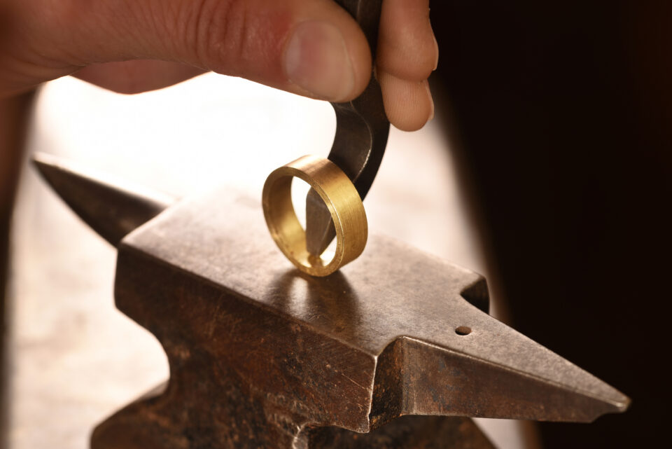 hand of a goldsmith punches a hallmark into a golden ring on an